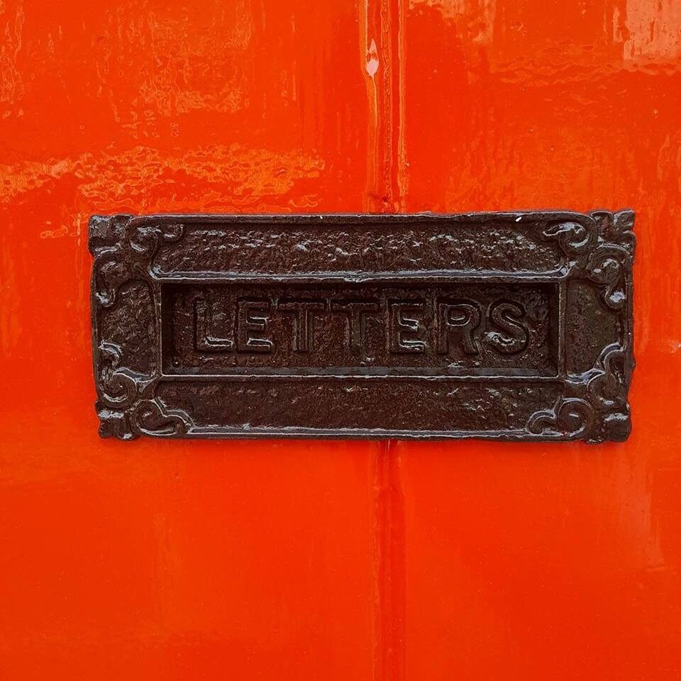 A cast-iron letterbox marked LETTERS on the orange-red shop door