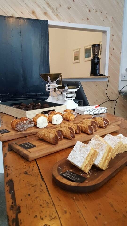 Cannoli and slices of mille-feuille on wooden boards on the counter, with old weighing scales behind